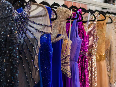 Formal evening dresses in multiple colors with sparkly embellishments displayed on black hangers including blue, gold, and purple gowns