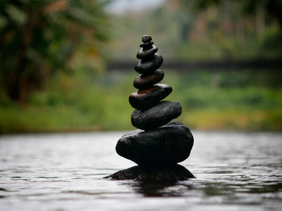 Balanced stack of smooth black stones in water with blurred natural background