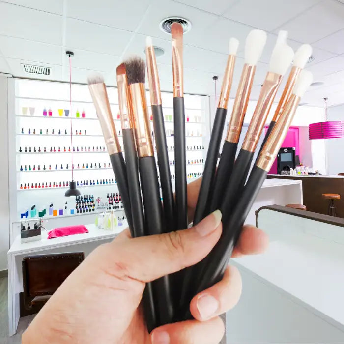 Professional makeup brushes with black handles and copper ferrules displayed in a modern salon setting with nail polish collections in the background.