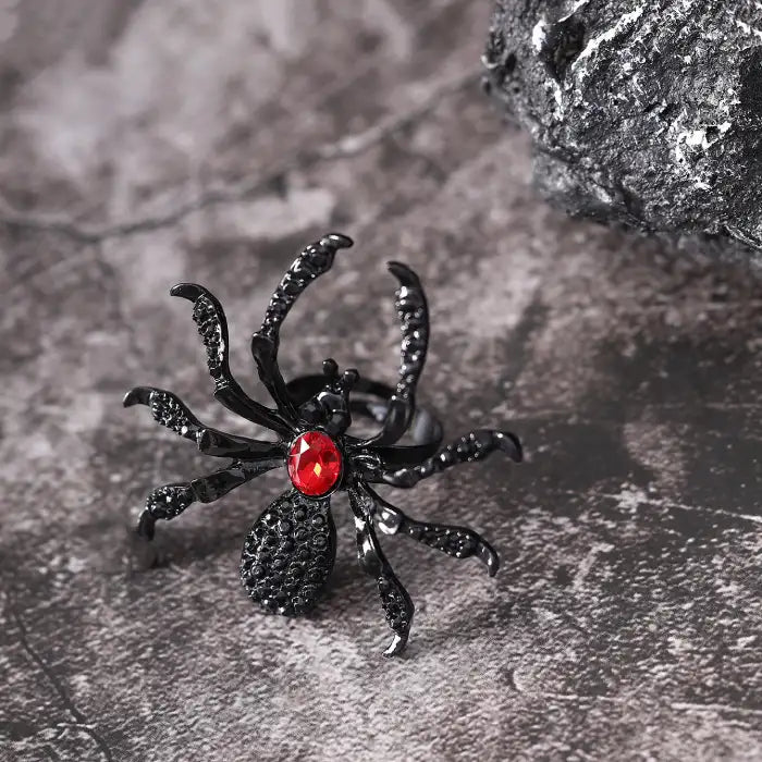Blackwidow Spider rings with red gem center and black textured body on stone surface