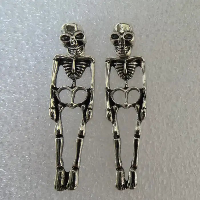 Gothic-style silver skeleton earrings on textured surface, showing full-body and skull features.
