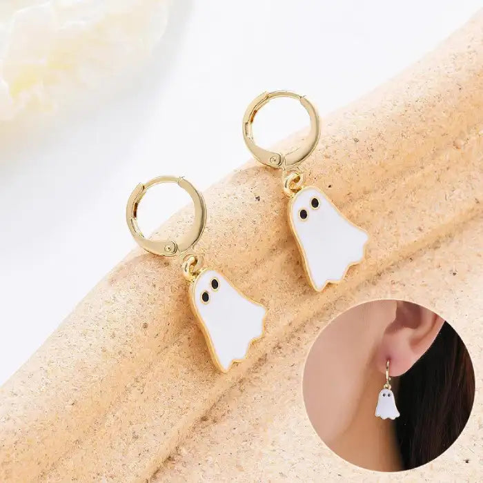 Halloween earrings with cute white ghost charms and gold hoops shown on display and worn on ear.