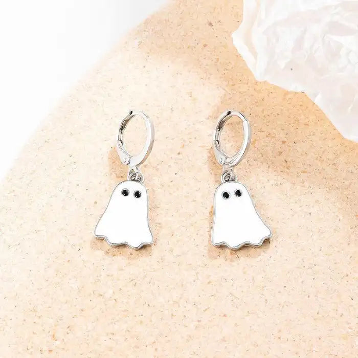 Silver hoop Halloween earrings with white ghost charms displayed on neutral textured surface.