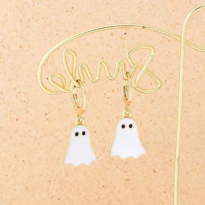 Halloween earrings featuring white ghost charms on gold hoops hanging on decorative holder.