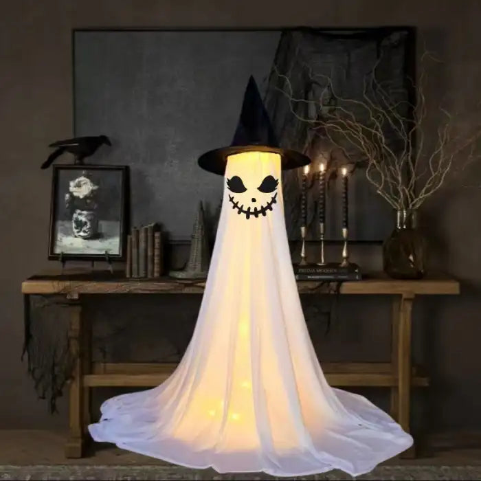 Halloween Ghost Yard Decor smiling stitched face ghost with witch hat glowing in dark setting.