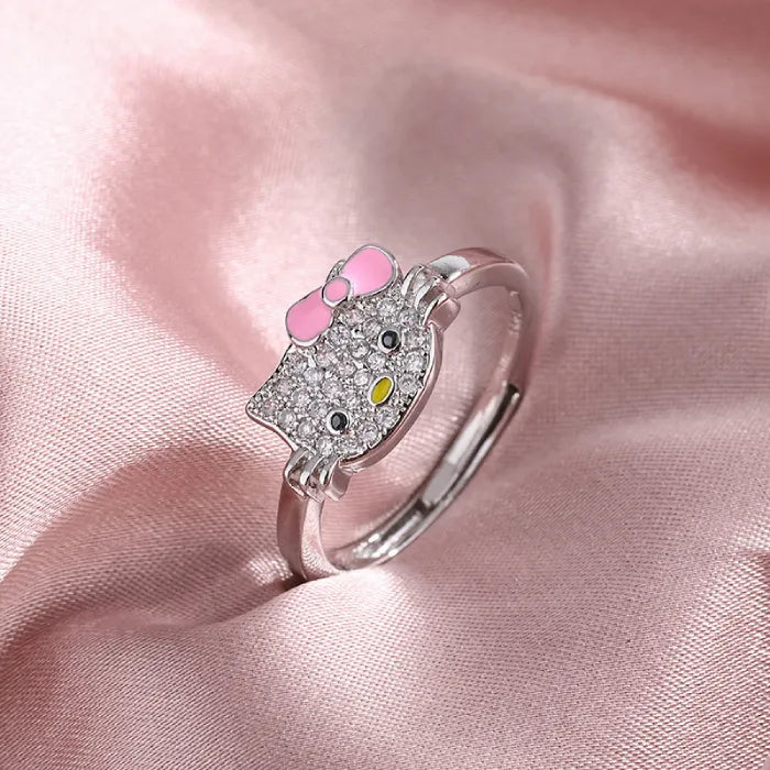 Hello kitty jewelry set ring with crystal face and pink bow displayed on soft pink satin fabric.