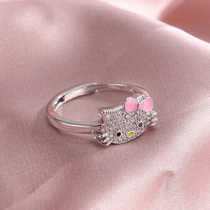 Hello kitty silver ring with pink bow and crystal face from jewelry set on pink satin background.