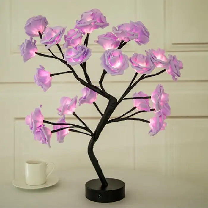 LED tree lamp with purple rose lights on black branches, placed on a white table with neutral background.