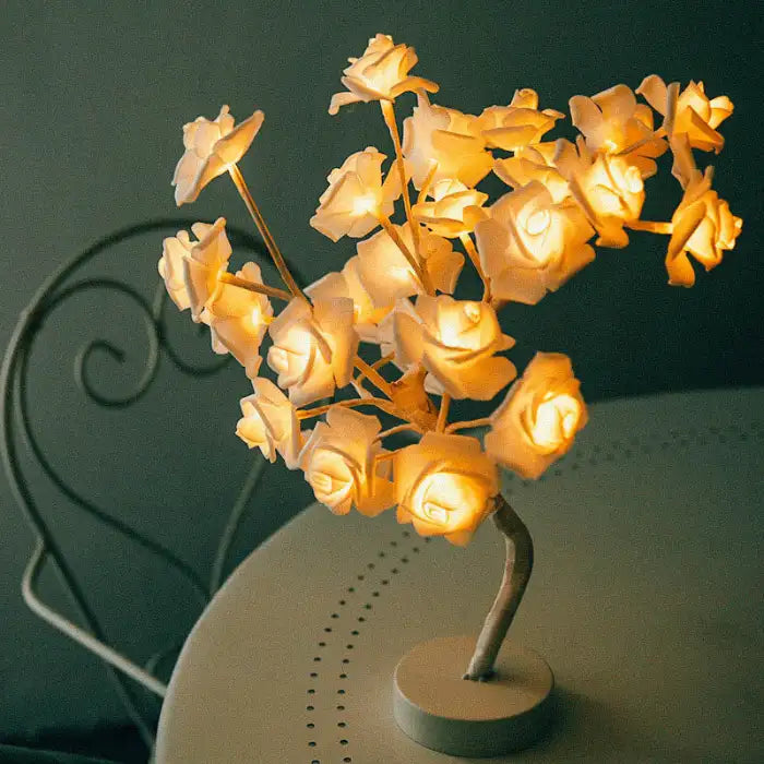 LED tree lamp with warm white rose flowers on a round table with a curled iron chair in cozy lighting.