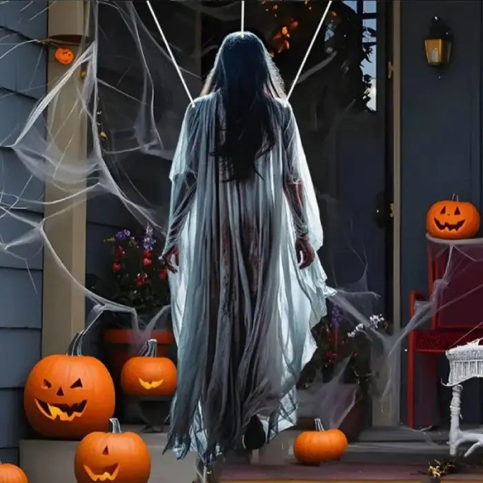 Life size Halloween prop of ghost woman with flowing white gown walking up decorated porch at night.