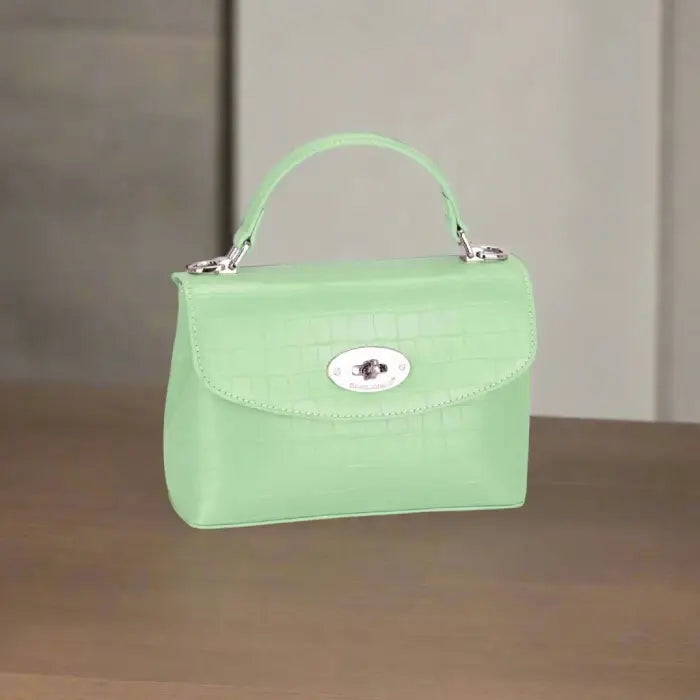 Mint green crocodile-textured handbag with silver clasp displayed on a wooden surface for style inspiration.