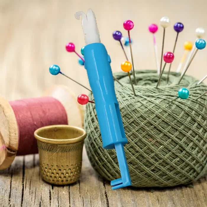 Needle threader with pins, thread spools, thimble, and yarn on rustic wooden background.