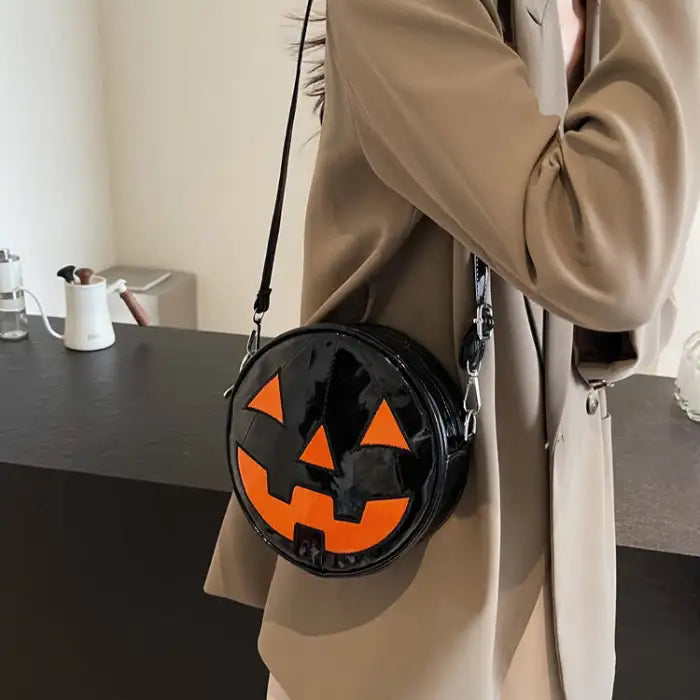 Pumpkin Head Purse in glossy black with bold orange jack-o-lantern face worn crossbody.