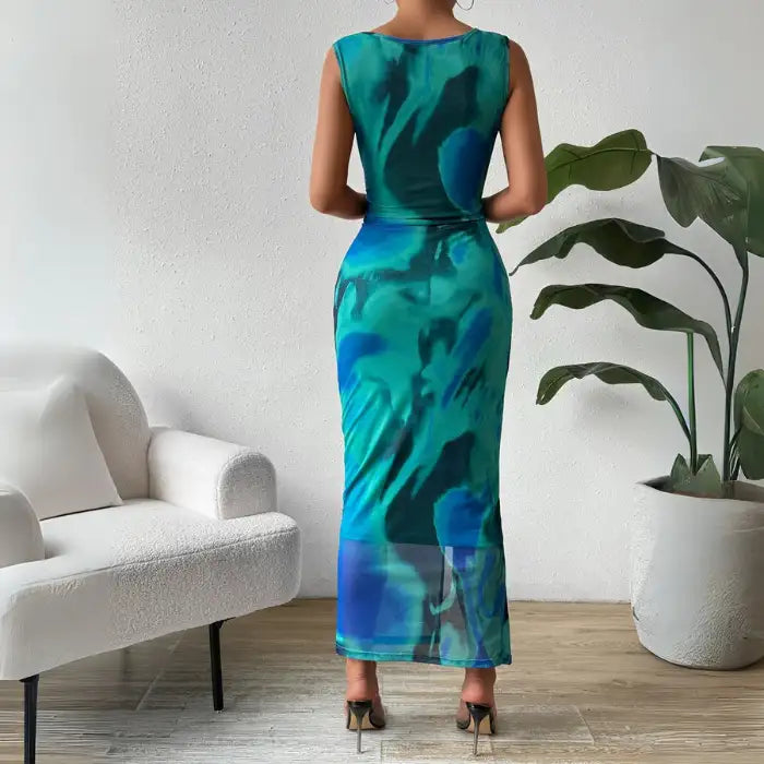 Back view of a green ruched maxi form-fitting dress with a sleeveless design and vibrant tie-dye print.