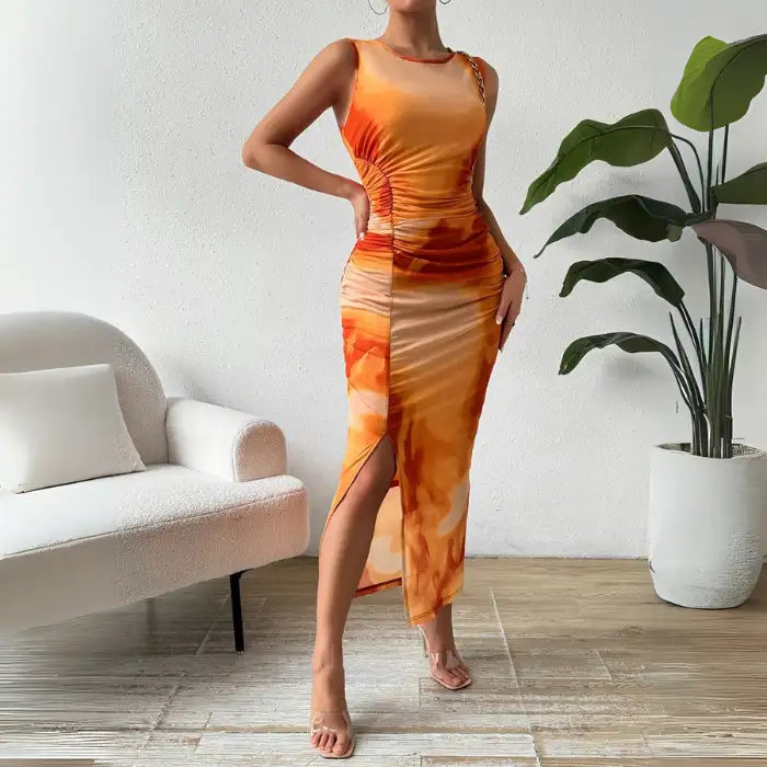 Ruched maxi form-fitting dress in orange with a sleeveless design and side slit, styled with clear heels.