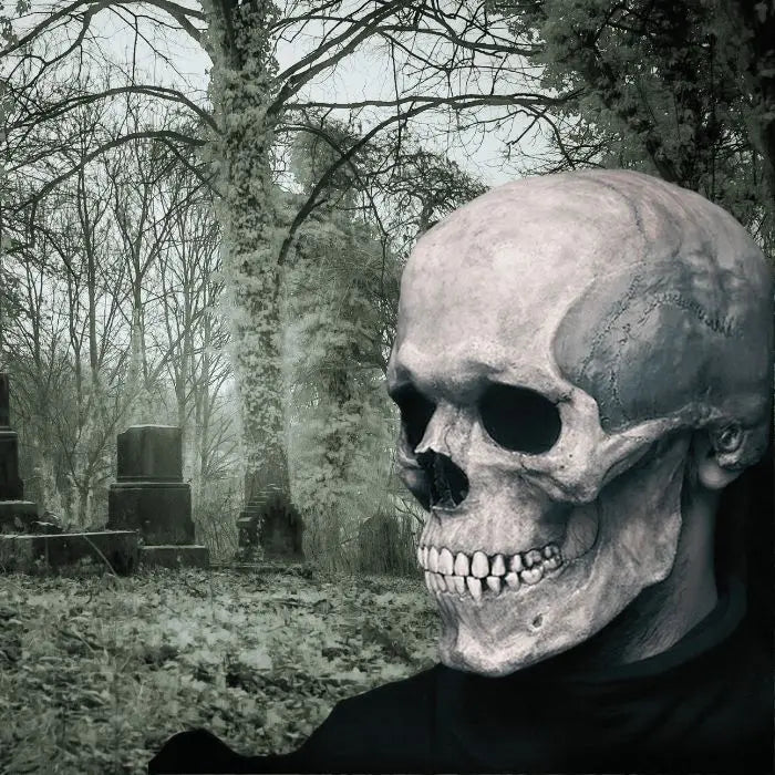 Side view of skull mask in foggy graveyard with tombstones and eerie forest backdrop.