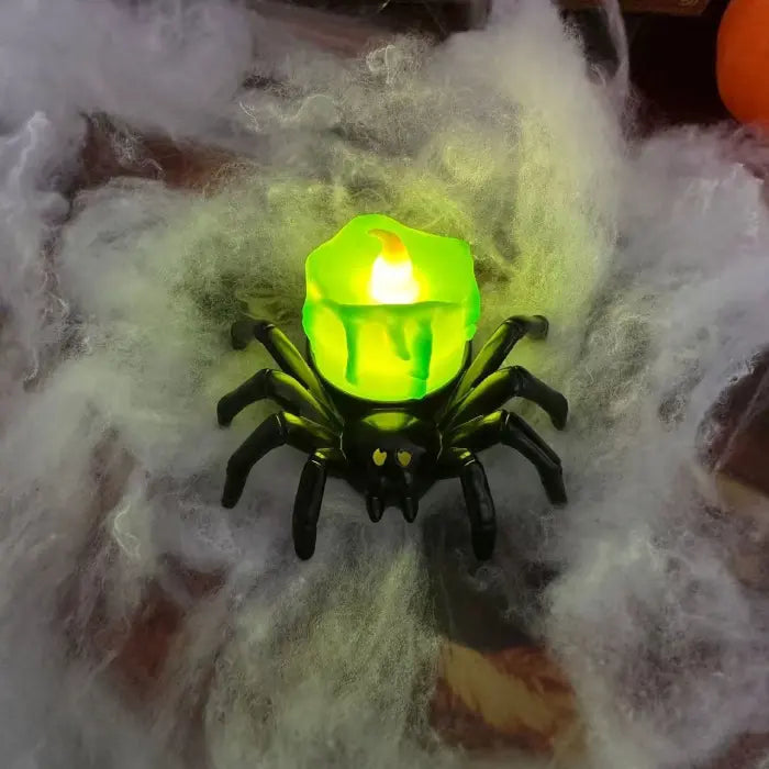Green LED spider candle glowing on white spiderweb Halloween decor background.