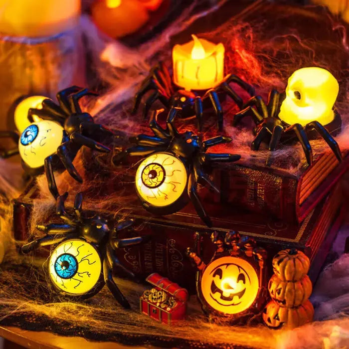 Halloween spider candle and skull lights displayed on books with cobwebs and pumpkins.
