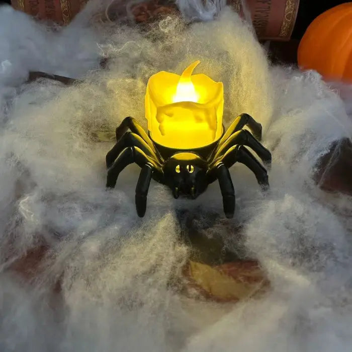 Spider candle with yellow LED flame surrounded by Halloween cobweb and pumpkin decor.