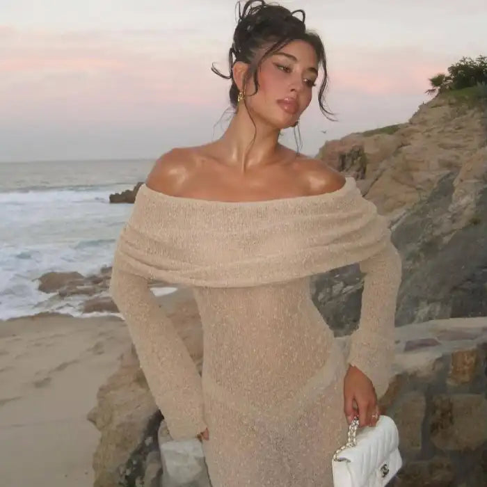 Women's one-shoulder long-sleeve knitted vacation dress in beige styled by the beach at sunset.