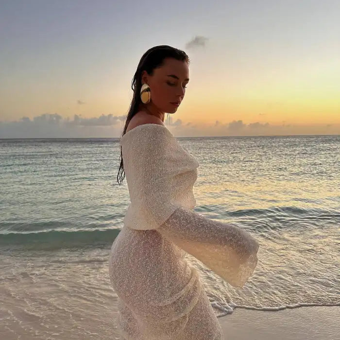 Women's one-shoulder long-sleeve knitted vacation dress in white captured at sunset by the beach