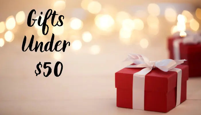 Gifts under 50 with red boxes and white ribbons in front of warm bokeh lights and soft festive glow.