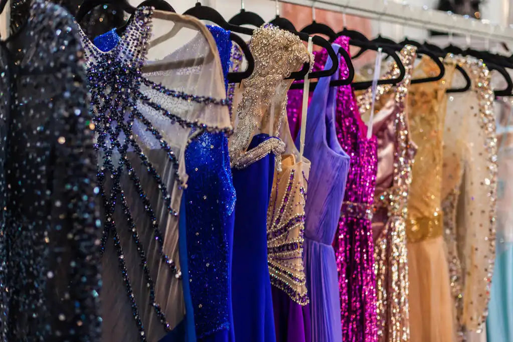 Formal evening dresses in multiple colors with sparkly embellishments displayed on black hangers including blue, gold, and purple gowns