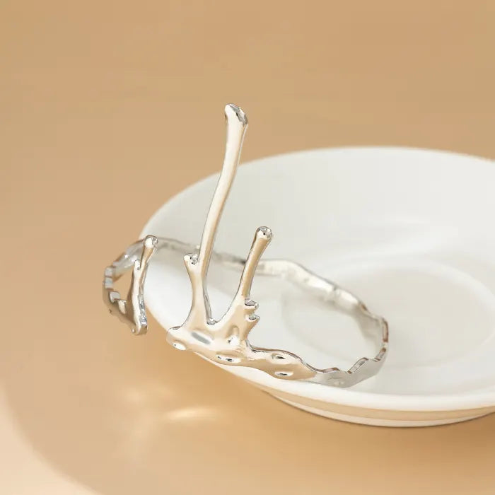 Silver branch-like decorative item on a white plate against a beige background