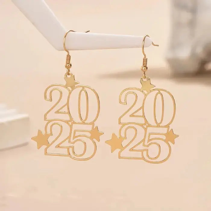 Gold New Year 2025 earrings displayed on white jewelry stand against neutral background