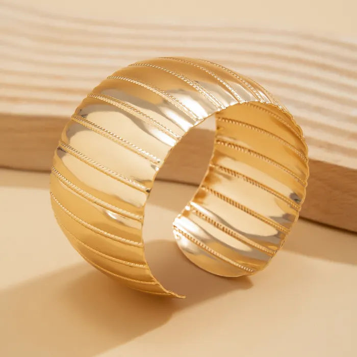 Gold bracelet with ribbed design on a beige background