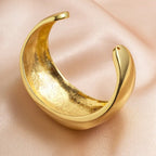 Gold crescent-shaped necklace on a soft pink fabric background