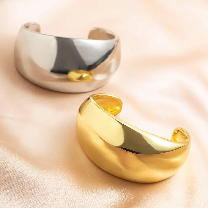 Gold and silver cuff bracelets on a soft pink background