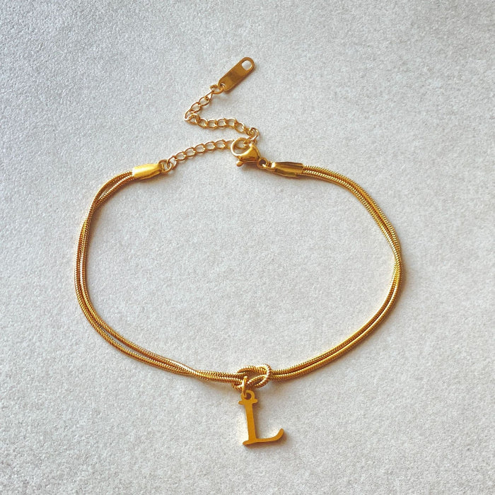 Gold bracelet with a letter 'L' charm on a light gray background