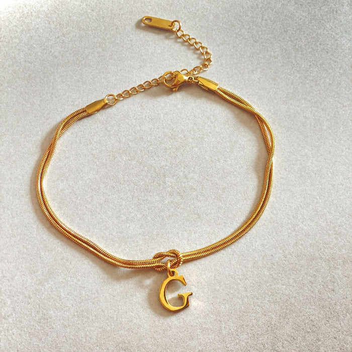 Gold bracelet with a 'G' charm on a light gray background