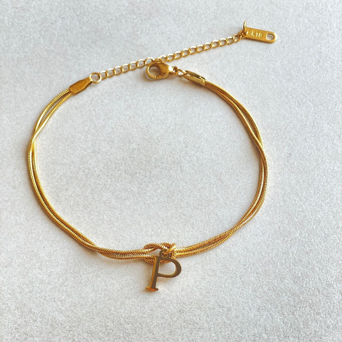 Gold bracelet with a letter 'P' charm on a light gray background