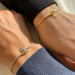 Two wrists wearing gold and silver bracelets on a neutral background
