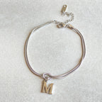 Silver bracelet with a gold letter 'M' charm on a light gray background