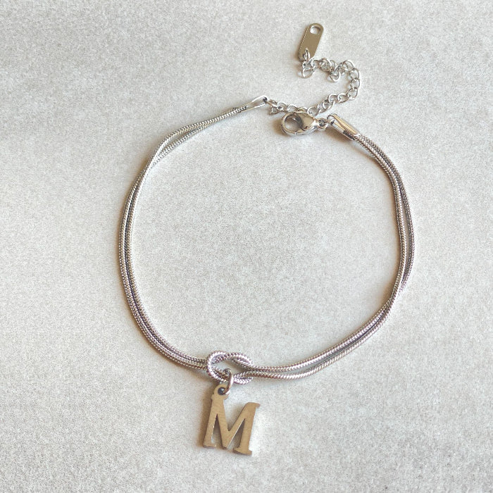 Silver bracelet with a gold letter 'M' charm on a light gray background