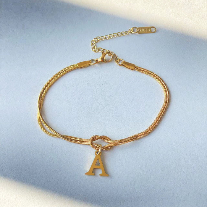 Gold bracelet with a letter 'A' charm on a light blue background