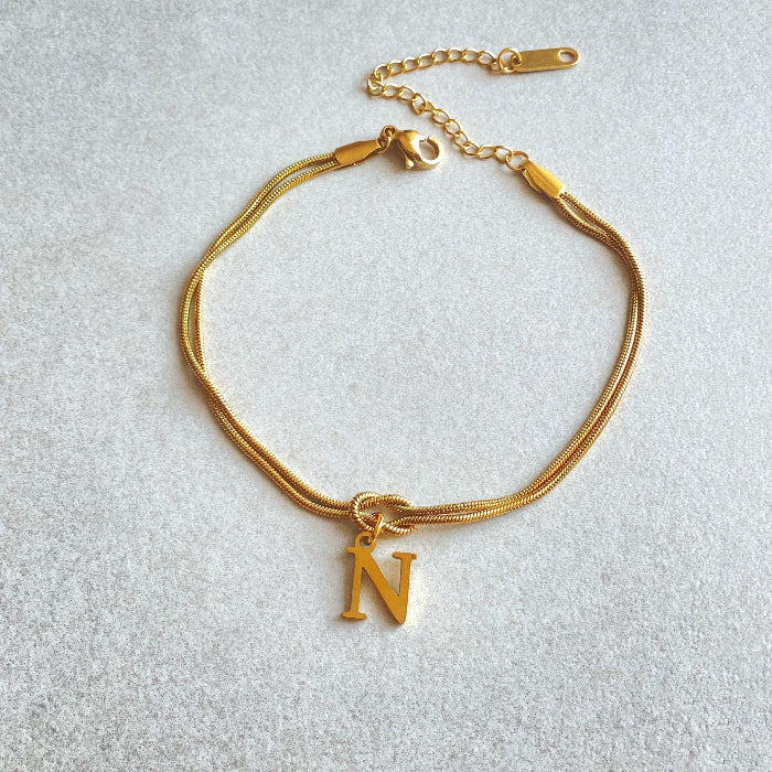 Gold bracelet with a 'N' charm on a light gray background