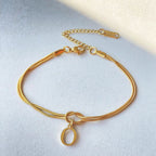 Gold bracelet with a knot design and small pendant on a light gray background