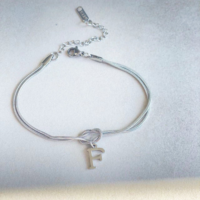 Silver bracelet with a knot and letter 'F' charm on a light gray background