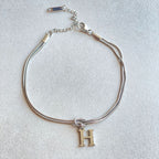 Silver bracelet with a gold 'H' charm on a light gray background