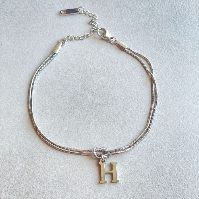 Silver bracelet with a gold 'H' charm on a light gray background