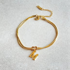 Gold bracelet with a 'M' charm on a light gray background