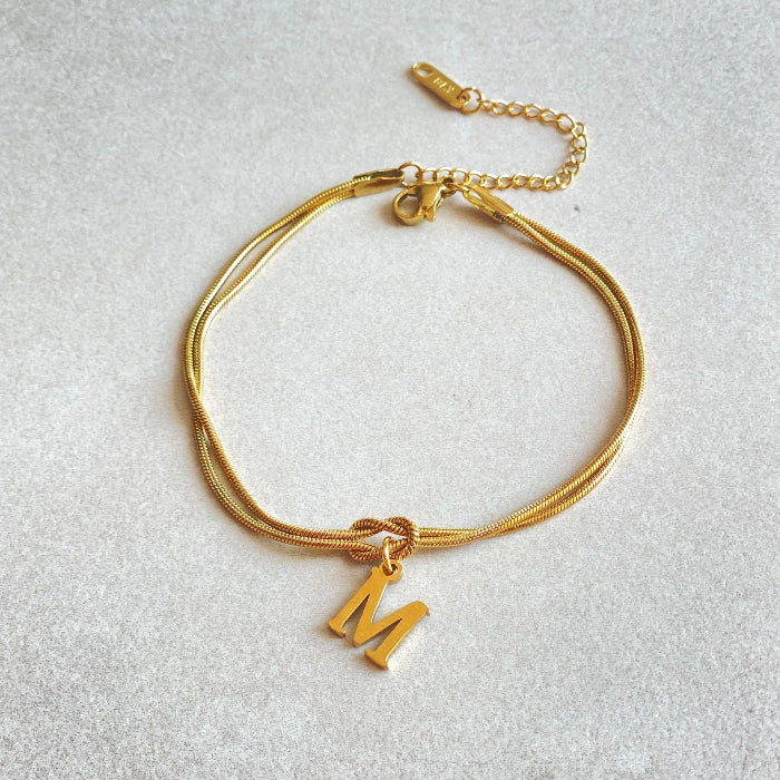 Gold bracelet with a 'M' charm on a light gray background