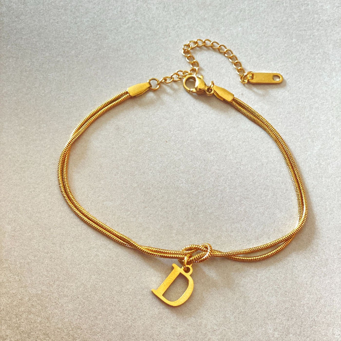 Gold bracelet with a 'D' charm on a light gray background