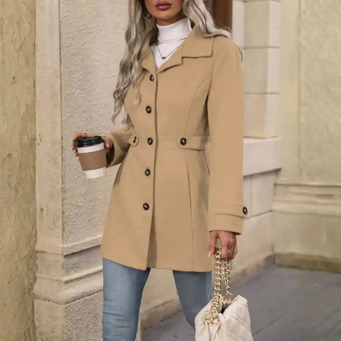 Woman wearing a beige trench coat holding a coffee cup and a handbag on a city street.