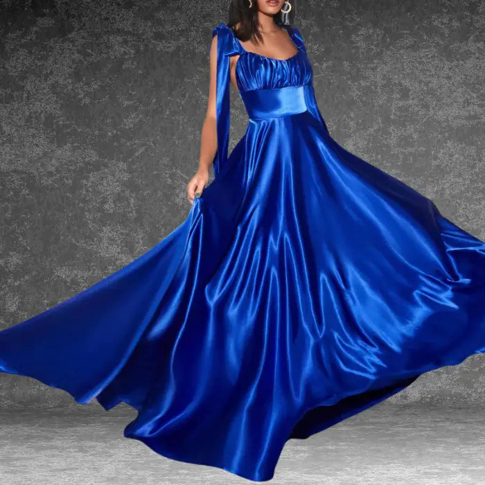 Model showcasing a stunning royal blue satin prom dress indoors. The long, flowing skirt and tie-shoulders create elegance.
