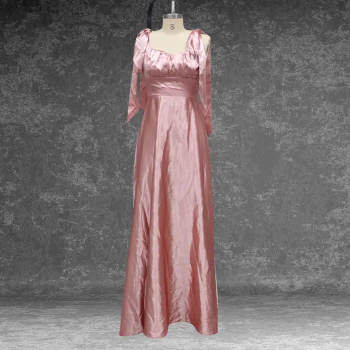 Soft blush pink satin prom dress presented on a mannequin. Showcases the romantic style with tie shoulders and ruched bodice.